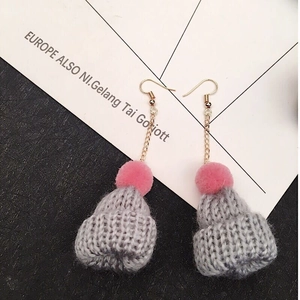 Detailed macro view of gray knitted Christmas hat earrings with pink pompom and gold chain