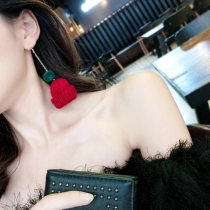 Detail of Christmas themed earring featuring green pompom and red knitted hat on a model