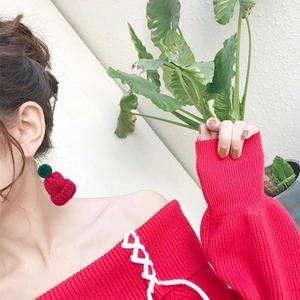 Detail of red knitted Christmas hat earrings with green pom-pom on female model