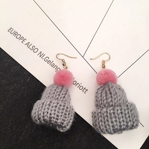 Macro detail of gray knitted Christmas hat earrings with soft pink pompom and gold hook
