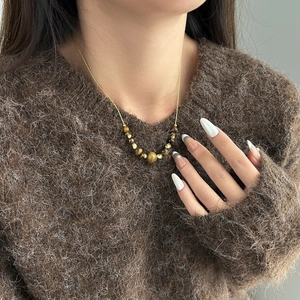 Elegante collana lunga dorata con ciondolo in pietra occhio di tigre su maglione marrone