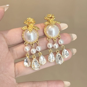 Dettaglio macro di orecchini vintage in oro con rose, perle e nappe di cristallo lucido
