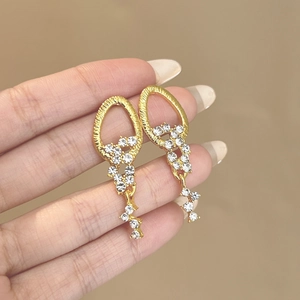 Dettaglio ravvicinato di orecchini pendenti dorati con strass brillanti in mano