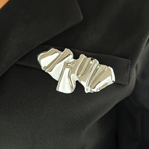 Silver angel-inspired brooch with pleated texture pinned on black suit fabric
