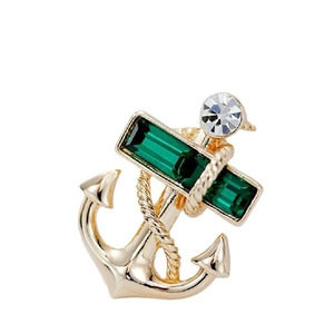 Detailed view of a golden anchor brooch with a green emerald gem and white diamond accent