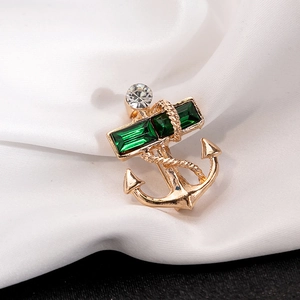 Detail of gold anchor brooch with green emerald-cut stones and clear rhinestones on white silk