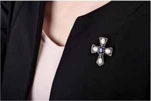 Detailed close-up of vintage cross brooch with blue crystal and pearls on a blazer