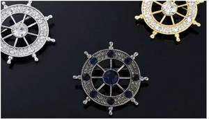 Macro view of crystal encrusted nautical helm brooches in silver, gold, and gunmetal