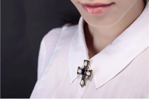 Vintage gold cross brooch with white pearls and blue gemstone worn on a white collar