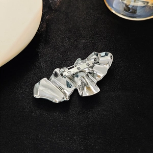 Macro shot of silver wave brooch back featuring secure metal pin clasp on black texture