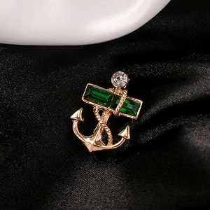 Close-up of gold nautical anchor brooch with green emerald-cut stones and rope detail