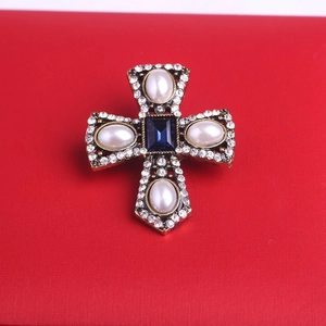 Detailed view of a baroque cross brooch with blue gems, pearls, and crystals on red