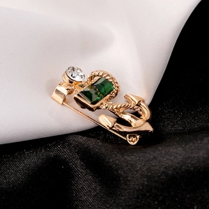 Detail view of a gold anchor brooch featuring emerald green crystals on silk fabric