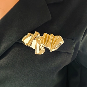 Macro detail of a golden irregular pleated brooch pinned to a black suit lapel