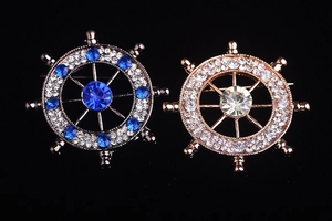 Detailed view of silver and gold nautical ship wheel brooches with sparkling crystals