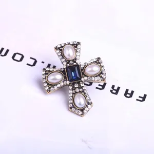 Macro detail of vintage gold cross brooch with blue gemstone and water-drop pearls