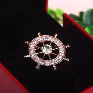 Macro shot of rose gold ship rudder brooch with sparkling crystals on red jewelry box