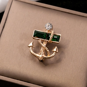 Detailed close-up of golden nautical anchor brooch with emerald green stones and twisted ropes