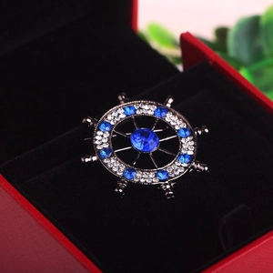 Detailed close-up of a vintage ship helm brooch with blue rhinestones in a gift box