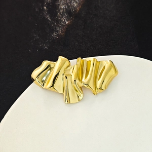 Macro shot of polished gold layered pleated brooch on a white stand with black background