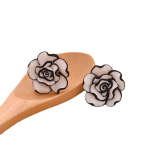 Minimalist white rose stud earrings with black edges on a natural wooden spoon
