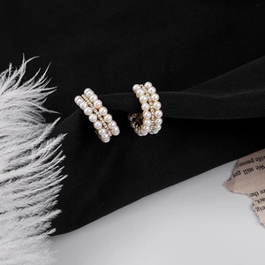 Detailansicht eleganter goldener C-Ohrringe mit Perlen und Strass auf schwarzem Stoffhintergrund
