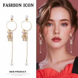 Detalle de pendientes largos dorados con oso de cristal y perla en una modelo