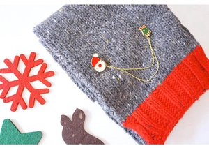 Détail de broches en émail Père Noël et cloche reliées par des chaînes sur un tricot