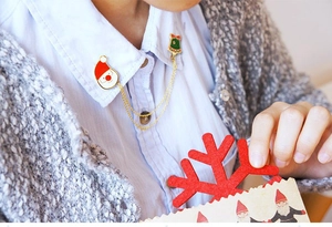 Détail d'une broche de col de Noël avec Père Noël et cloche sur chemise bleue