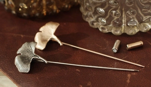Detailed close-up of silver and antique gold ginkgo leaf pins on textured leather