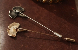Detailed close-up of golden and silver ginkgo leaf lapel pins on a premium leather base