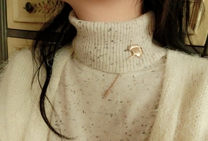 Golden ginkgo leaf brooch detail on white turtleneck sweater with elegant leaf vein textures