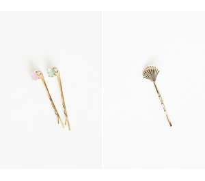 Détail de deux pinces à cheveux dorées avec strass et design de coquillage sur blanc