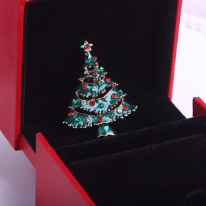 Détail macro d'une broche sapin de Noël en émail et strass dans un coffret cadeau rouge