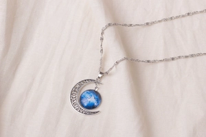 Detailed shot of crescent moon necklace with blue nebula pendant on soft beige linen fabric