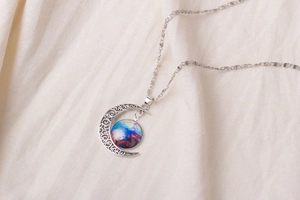 Detailed shot of a silver moon necklace with colorful nebula glass gem and hollow patterns