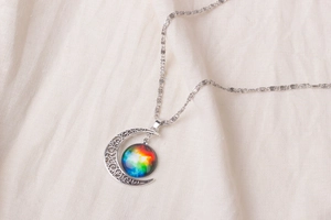 Macro shot of silver crescent moon necklace with colorful cosmic nebula sphere detail