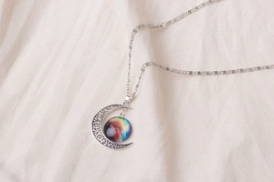 Macro shot of silver crescent moon pendant with nebula glass on beige linen fabric