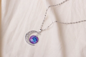 Macro detail of crescent moon pendant with purple galaxy glass orb on linen fabric