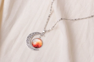 Detailed shot of moon pendant with starry nebula inlay on a soft fabric background