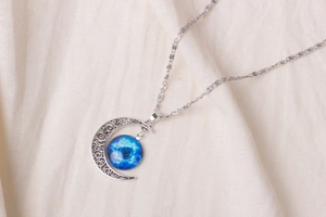 Close-up of crescent moon pendant with blue starry sky glass ball on linen background