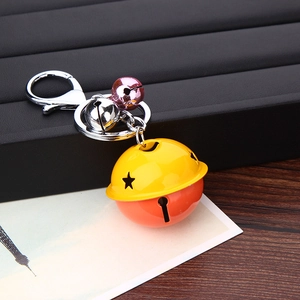 Detail of bicolored bell keychain with star cutouts and pink accent bells on wood surface