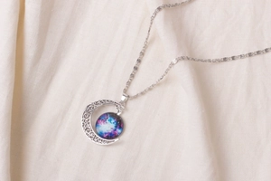 Detailed macro of a crescent moon pendant with galaxy nebula gemstone on soft fabric