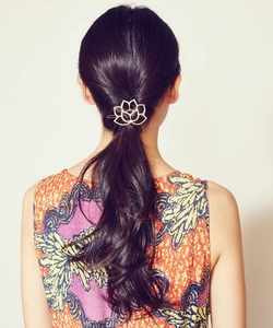Detail view of a gold lotus flower metal hair clip worn on a low ponytail style