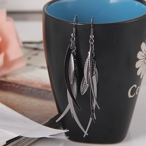 Dettaglio ravvicinato di orecchini a foglia d'argento appesi a una tazza da caffè