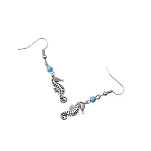 Gros plan de boucles d'oreilles hippocampe argentées avec perles turquoise et gravures