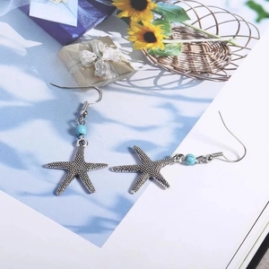 Détail macro de boucles d'oreilles étoiles de mer argentées avec perles turquoise