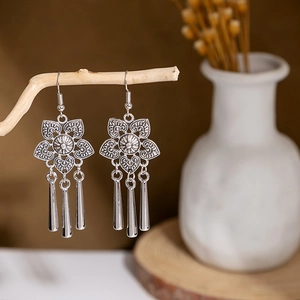 Ethnic silver-toned hollow flower earrings with sleek fringe tassels on a wooden display