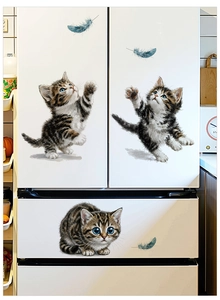 Close-up of adorable tabby kitten decals and blue feathers on a white refrigerator surface