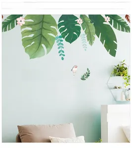 Détail de feuilles de monstera tropicales et stickers oiseaux sur un mur bleu clair